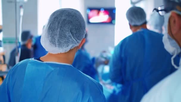 手術室の外科医のチームワーク 手術中にモニターの画面を見ている医師の裏側のビュー メディカルコンセプト — ストック動画