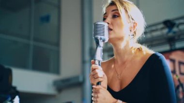 Çekici bir kadın mikrofona şarkı söylüyor. Profesyonel şarkıcı mikrofonun başında duruyor ve canlı müzik yapıyor. Yavaş çekim.