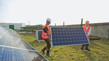 Güneş panellerinin kurulumu. Yazın mavi güneş pili taşıyan koruyucu üniformalı işçiler. Sürdürülebilir yeşil enerji.