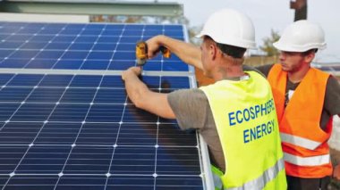 Fotovoltaik güneş panelleri kuran işçiler. Beyaz kasklı adamlar güneşli bataryaları yüklüyorlar. Yenilenebilir enerji kaynağı.
