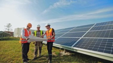 Güneş panelleri kurulumu planını inceleyen işçiler. Koruyucu üniformalı ve güneş çiftliğinde çalışan adamlar. Yenilenebilir enerji.