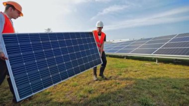 İşçiler çimlerin üzerine kurmak için güneş paneli taşırlar. Çiftlikte güneşli bataryalarla çalışan teknisyenler. Alternatif yeşil enerji.