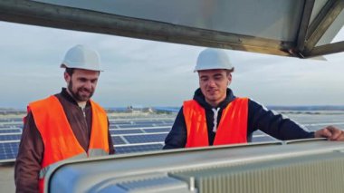 Güneş jenerasyonu teknolojileri. Koruyucu üniformalı erkek işçiler modern bir elektrik çiftliğinin arka planına güneş panelleri kurmayı sağlıyorlar..