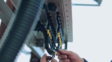İşçi eli elektrik ekipmanını bağlar. Dışarıdaki elektrik sistemine siyah kablolar bağlayan elektrikçi..