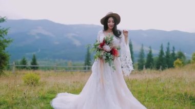 Dağlarda yaşayan lüks bir gelin. Uzun beyaz elbiseli, şapkalı ve çiçekli güzel bir kadının uzun bir portresi..