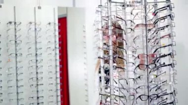 Optik mağazasındaki güzel, uzun saçlı kadın. Yeni gözlükleriyle standın yanındaki şık gözlüklü güzel, gülümseyen genç bayan..