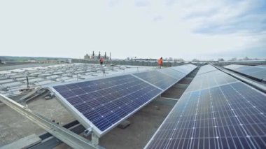 Çatıda bir sürü güneş paneli var. İşçiler güneşli piller kuruyor. Güneş enerjisi üretim tesisinin düzenlenmesi