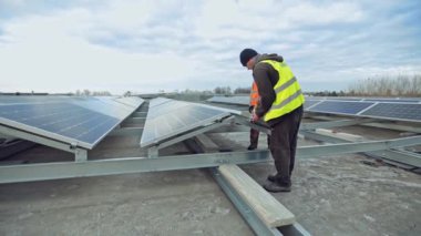 Güneşli batarya kurulumu. İşçiler büyük bir binanın çatısına güneş panelleri kuruyor. Yeşil alternatif enerji.