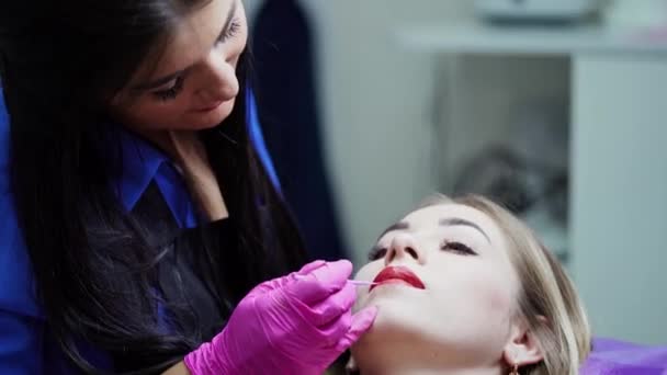 女性化粧師が唇に化粧をしている サロンでクライアントの唇の化粧品の手袋のプロフェッショナルな美容師 — ストック動画