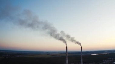 Arka planda duman olan iki boru. Akşamları tarlalar ve ormanlar arasında dumanlı sanayi boruları.