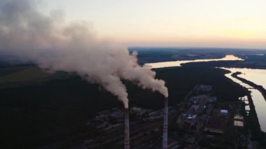 Doğal çevredeki borulardan beyaz duman çıkıyor. Akşamları kırsal bölgedeki güzel nehrin yanındaki sanayi fabrikası. Hava kirliliği.