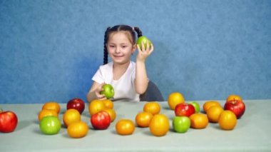 İçerde meyveleri olan küçük tatlı bir kızın portresi. Masada olgun meyve var. Güzel gülümseyen çocuk masada taze elmalarla oynuyor..