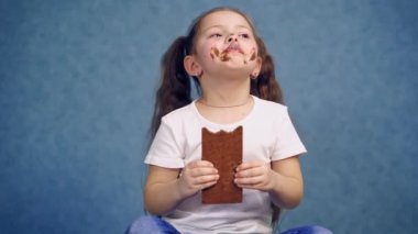 Çikolata yiyen edepsiz kız. Komik çocuk elinde çikolatayla stüdyoda izole edilmiş tatlı bir parçayı ısırıyor. Neşeli çocukluk.