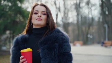 Çekici kadın elinde plastik bardakta kahve tutuyor. Kürk mantolu güzel bir kızın portresi şehir parkında eli olan birini arıyor. Yavaş çekim.