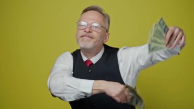 Elinde parası olan mutlu yaşlı bir adam. Dolarlar yaşlı, neşeli bir adamın ellerinde. İş adamı sarı stüdyoda parayla dans ediyor. Yavaş çekim.