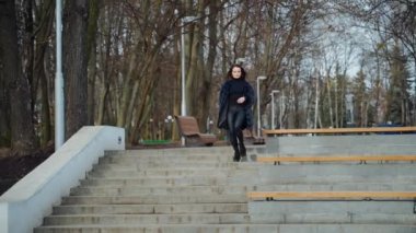 Parktaki güzel kız. Mutlu genç bayan parkta merdivenlerden aşağı iniyor. Kürk mantolu çekici bir model. Yavaş çekim.