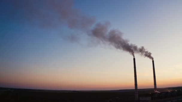 夕方の空の背景に煙が付いているパイプ 日没時に工場の2つの工業用パイプから空中に入る有害な煙 — ストック動画