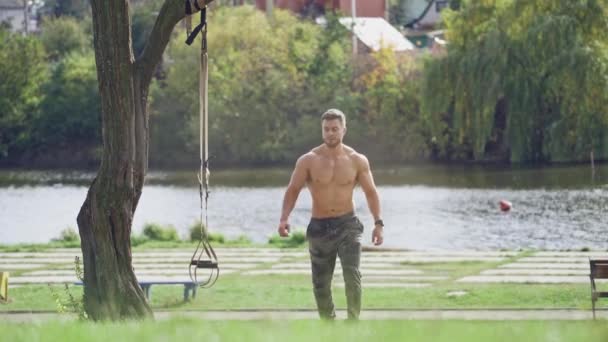 健康なスポーツマンは屋外トレックスのトレーニングを開始します 晴れた日の川の背景にストラップ付きアクティブアスリートトレーニング — ストック動画