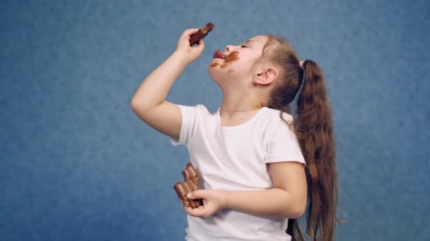 かわいい女の子は屋内でチョコレートを舐めている おいしいお菓子を食べて汚れていきます 小さな子供はチョコレートで塗られています — ストック動画