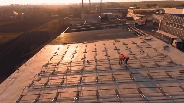 在一座建筑物的屋顶上建造太阳能农场 工人们在日落时为太阳能电池板安装金属结构 空中景观 — 图库视频影像