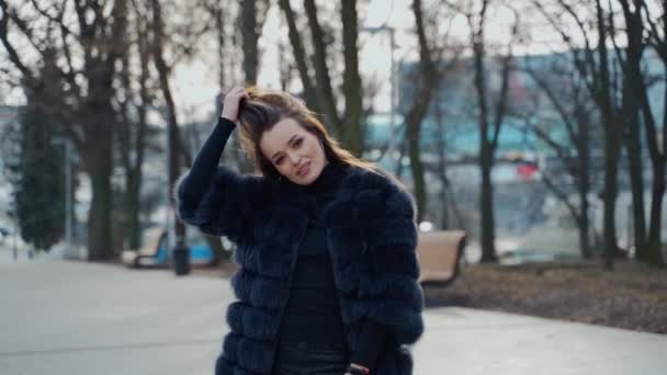 屋外のセクシーな女の子の肖像画 公園の高級毛皮のコートに魅力的な女性 市街地の背景にある美しい若いモデル スローモーション — ストック動画