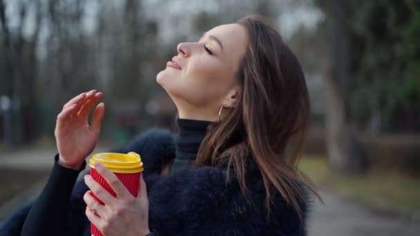 冬の美しい女性のプロフィール 長い髪の魅力的なブルネットは屋外で熱い飲料が付いているプラスチック カップを握ります スローモーション — ストック動画