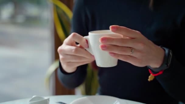 女性の手でコーヒーを飲むホワイトカップ カフェでホットドリンクを楽しんでいる美しい若い女性 スローモーション — ストック動画