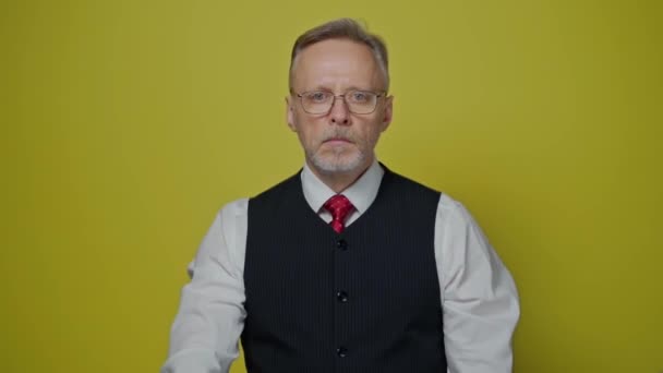 一个严肃的资深商人的画像 戴眼镜 留着灰胡子的成熟男人站在黄色的背景上 看着相机 — 图库视频影像