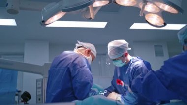 Ameliyathanede cerrahi işlem. Mavi üniformalı başarılı doktorlar klinikteki bir hastaya tıbbi aletlerle ameliyat yapıyorlar..