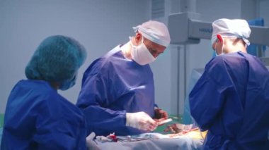 Cerrahların ekip çalışması ameliyathanede. Bir grup doktor hastaya ameliyat yapıyor. Ameliyat sırasında doktorun elleri steril eldiven ve kanla dolu..