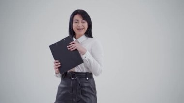 Güzel esmer bir kadının portresi. Beyaz bluzlu çekici bir kadın elinde siyah bir klasör tutuyor ve gülümseyen yüzünü ışığa kapatıyor. Yavaş çekim.