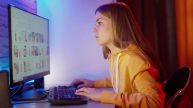Bilgisayarda çalışan bir kızın yan görüntüsü. Çekici genç bir kadın monitörün önünde oturuyor ve bazı bilgiler arıyor..