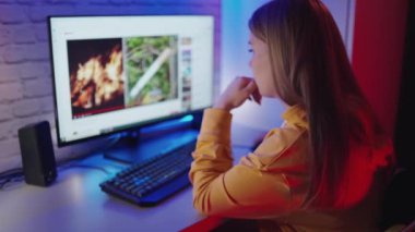Bilgisayarda video izleyen genç bir kadın. Evde monitörün önünde oturan konsantre bir kızın yan görüntüsü..