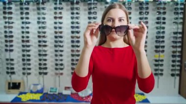 Gülümseyen genç kadının portresi yeni güneş gözlüğü taşıyor. Optik mağazasındaki güzel bir kızın ellerinde şık siyah bir gözlük..
