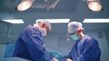 Cerrahların çalışma sürecinin yan görüntüsü. Mavi üniformalı erkek doktorlar modern ameliyathanede ameliyat yapıyorlar..