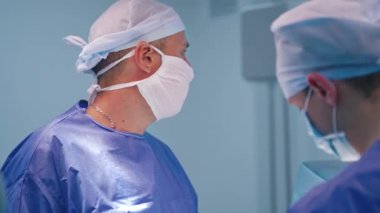 Ameliyat sırasında profesyonel bir doktorun portresi. Mavi üniformalı erkek cerrahlar ve hastane maskeleri. Yakın plan..