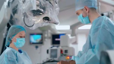Doktor ve asistanı ameliyathanede. Tıbbi üniforma uzmanı ameliyattan önce mikroskobu özelleştirir. Tıbbi konsept.