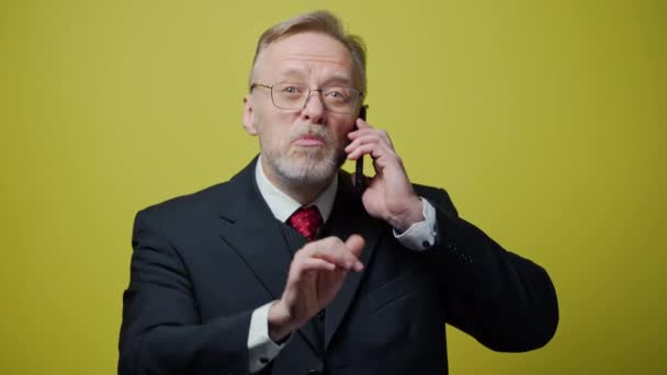 ハッピーシニアビジネスマンが電話をかける 携帯電話で話す黒い衣装の成熟した男の肖像画と黄色で隔離された多く — ストック動画