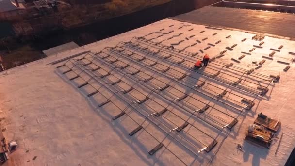 日没時に屋上に太陽光発電所を設置する 太陽電池パネルのための屋根に金属基盤を取付けるオレンジの均一の労働者 エアリアルビュー — ストック動画