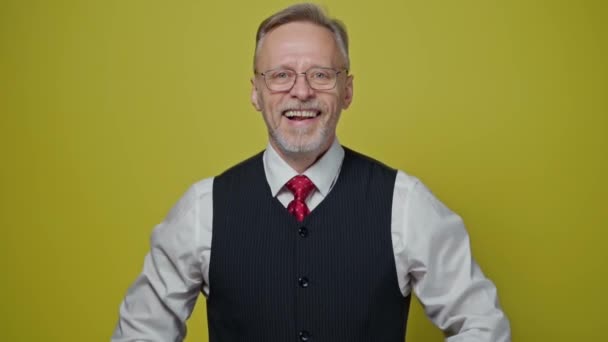 古いビジネスマンの笑顔の肖像 黄色い背景のカメラで笑っているメガネの成熟した男 ポジティブな感情 — ストック動画