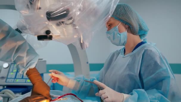 クリニックでの作業プロセス 外科医に医療機器を提供する女性アシスタント 医師は手術中に現代の顕微鏡を使用しています — ストック動画