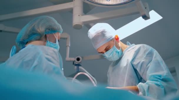 医者と看護師が手術をしている 医用制服とマスクの若い外科医は 患者に手術を行う 女性アシスタントがクリニックの専門家を支援 — ストック動画