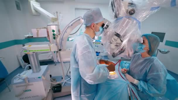 顕微鏡を介して患者に手術を行う外科医 現代の手術キャビネットの背景にある青い保護ユニフォームの医師 — ストック動画