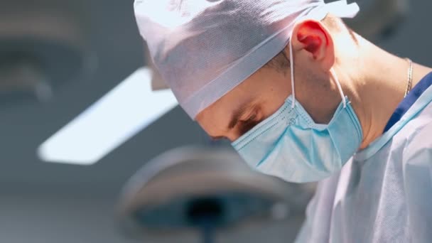 男性外科医が手術をしています 医師は医療機器を患う患者に手術を行う医療マスクに直面しています クローズアップ — ストック動画