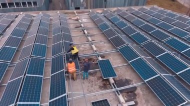 Düz bir çatıya güneş panelleri kuruluyor. Koruyucu üniformalı işçiler sıraya dizilmiş güneşli bataryaları yerleştiriyorlar. Güneşten gelen temiz enerji. Hava görünümü.