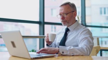 Laptopun önünde üzgün, olgun bir iş adamı. Beyaz gömlekli, kravatlı, çay ya da kahve içen ve ofiste bilgisayar başında çalışan gri saçlı bir adam..