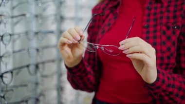 Kadınların elinde şık gözlükler var. Kadın alıcı optik mağazada yeni gözlük tutuyor. Yakın plan..