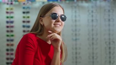 Moda güneş gözlüklü güzel kız. Gülümseyen genç kadın optik bir dükkanın bulanık arka planında yeni siyah gözlük deniyor..