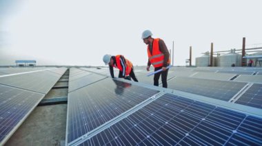 Mühendisler yeni bataryalar kuruyor. Üniformalı iki işçi güneş çiftliğine fotovoltaik paneller kuruyor..