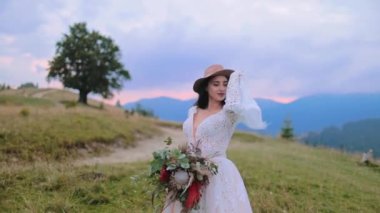Dağlarda yaşayan muhteşem bir gelin. Şapkalı, beyaz elbiseli, kolları sallanan ve doğada buket tutan güzel bir kadın..